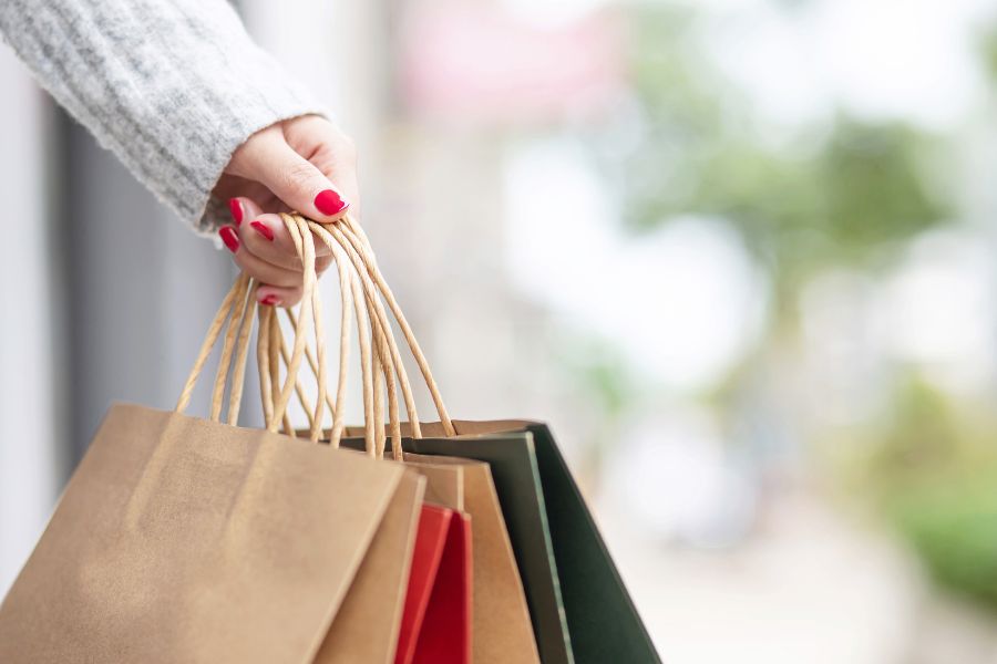 Woman with red nail polish holding four shopping bags to indicate impulse purchases
