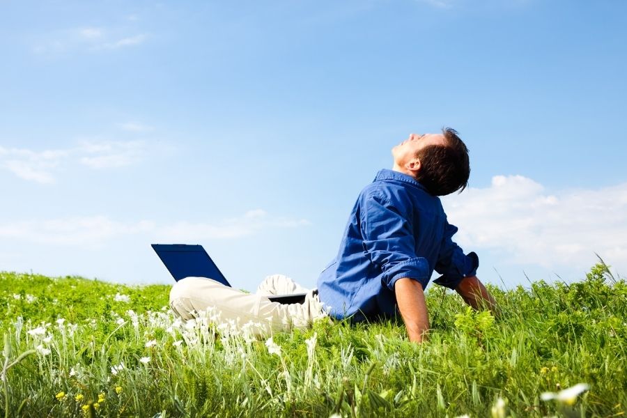 man working with laptop in meadow blue skies
