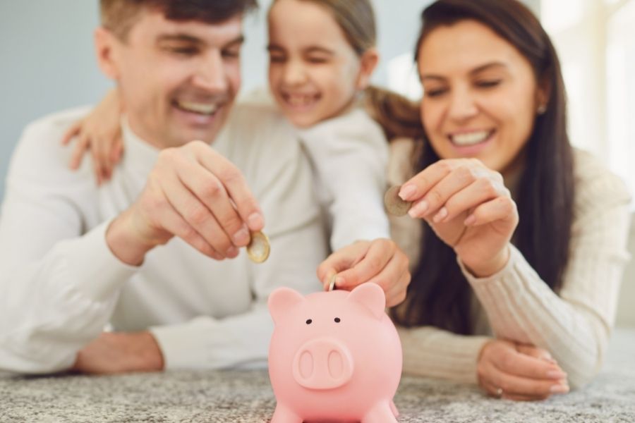 parents and daughter putting money into piggy bank