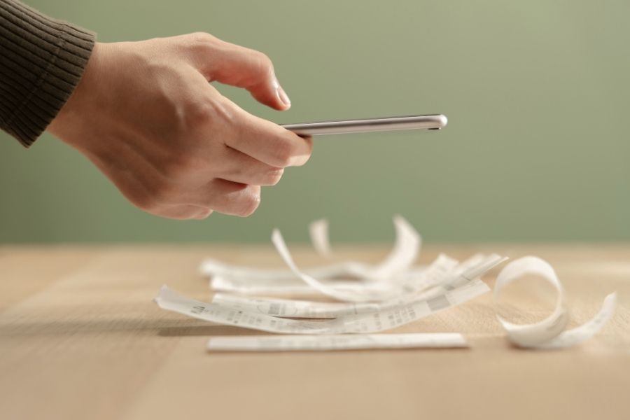 Hand using smartphone calculate paper receipts on table. Calcula